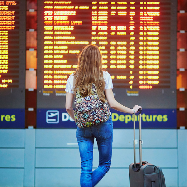A girl holding a trolley bag is watching the flight's timetable