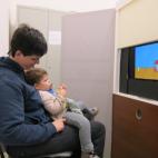 Neurocognitive Lab: a baby sitting on his mother's lap is looking at an image on a screen.