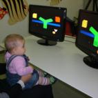 Laboratorio Neurocognitivo: un bambino seduto in braccio alla sua mamma esegue un esperimento di fronte a due monitor.