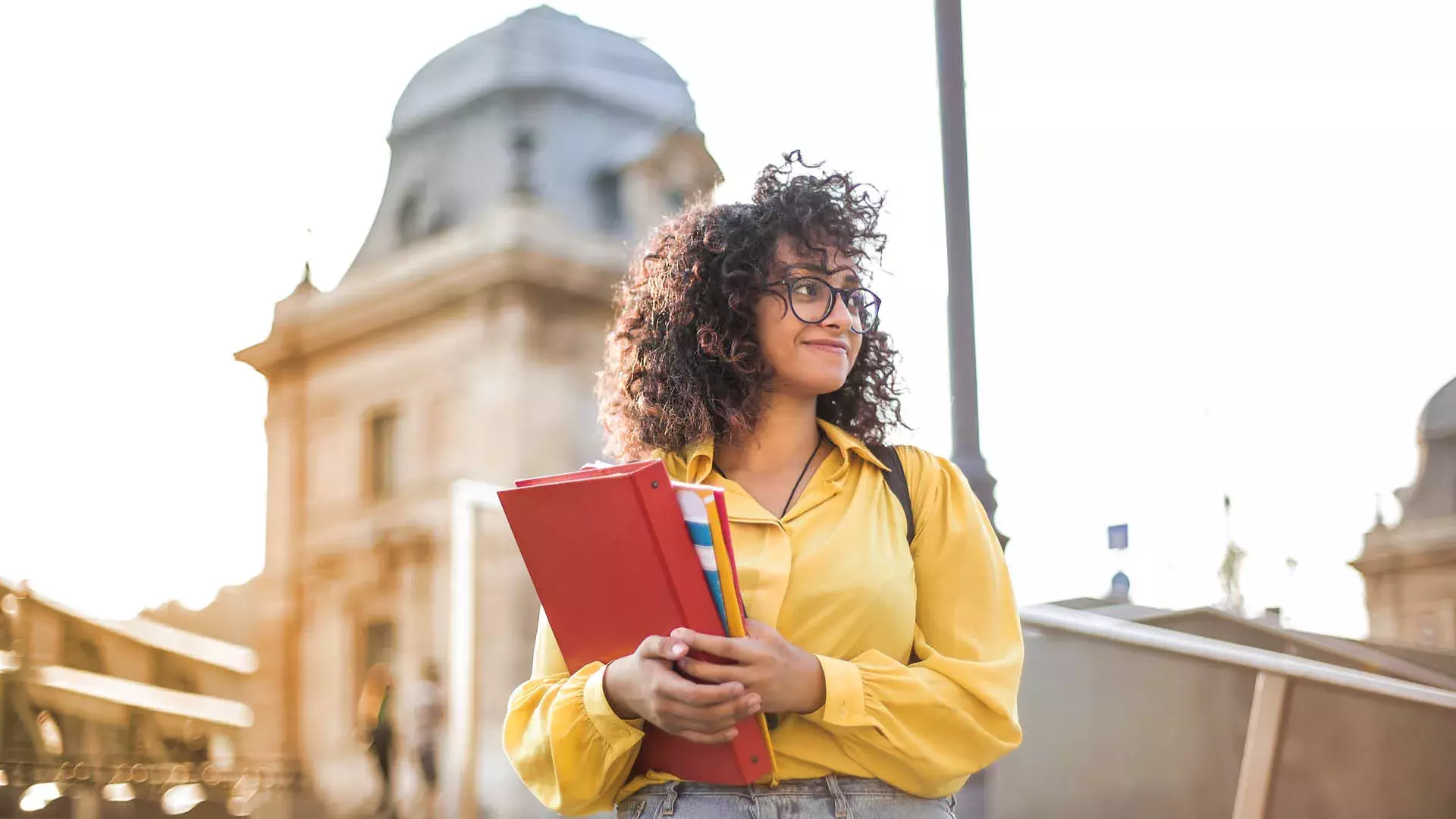 Ragazza con libri e camicia gialla in una città che sorride